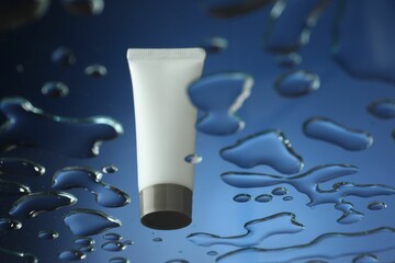 Moisturizing cream in tube on glass with water drops against blue background, low angle view. Space...