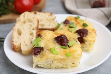 Tasty sausage casserole with green onion and bread on grey table, closeup