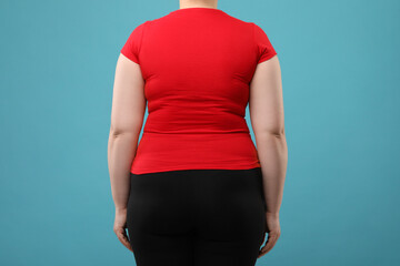 Overweight woman on light blue background, back view