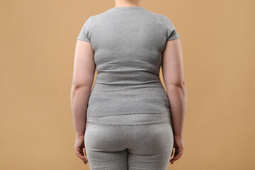 Overweight woman in grey clothes on beige background, back view