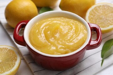 Delicious lemon curd in bowl and fresh citrus fruits on table, closeup