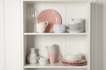 Different ceramic dishware and glasses on shelves in cabinet indoors