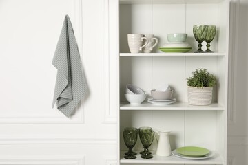 Different clean dishware and houseplant on shelves in cabinet indoors