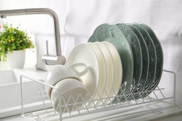 Drainer with different clean dishware and cups on white table in kitchen