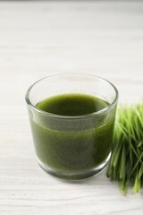 Wheat grass drink in glass and fresh sprouts on white wooden table, closeup