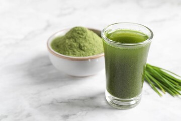 Wheat grass drink in shot glass on white marble table, closeup. Space for text