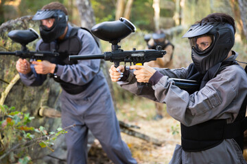 Paintball players aiming and shooting with guns at opposing team outdoors