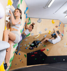 Focused young girl ascending colorful holds on indoor bouldering wall, demonstrating physical...