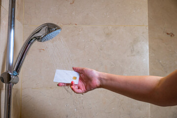 Person showers holding credit card by plumbing fixture