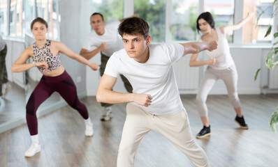 Cheerful active young Hispanic guy enjoying contemporary energetic dance at group class in light mirrored studio..