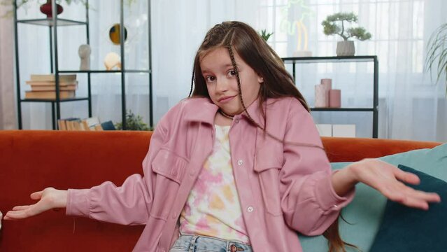 I don't know what to say. Confused young girl child feeling embarrassed about ambiguous question, having doubts, no idea, being clueless and uncertain. Teen kid sitting on couch in living room at home