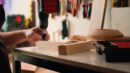Craftsperson changing power drill head into suitable one for task ahead, making holes into lumber...