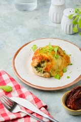 Baked chicken fillet stuffed with spinach, cheese and sun-dried tomatoes on a ceramic plate on a gray concrete background. Spinach recipes.