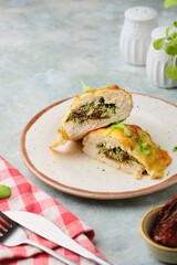 Sliced baked chicken fillet stuffed with spinach, cheese and sun-dried tomatoes on a ceramic plate on a gray concrete background. Spinach recipes.