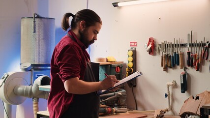 Carpenter drawing blueprints on notepad in studio, transforming creative ideas into tangible wood...