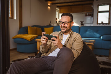 Adult man with eyeglasses play video games on his phone at home
