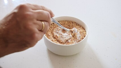 Caucasian Man Preparing Bowl of Oatmeal Mixed with Natural Yoghurt for Healthy Balanced Diet Breakfast