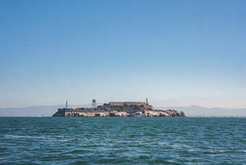 Fototapeta premium Alcatraz Island, San Francisco Bay, California, USA. Former federal prison, rocky, barren island with aged buildings. Water tower, lighthouse, blue waters, hills, sunny sky, isolation theme.