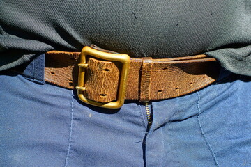 military old leather brown retro with yellow iron heavy buckle men's belt fastened on blue work...