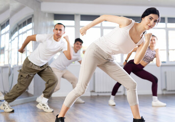 Group of young happy women and men in sportswear performing contemporary street dance in training room