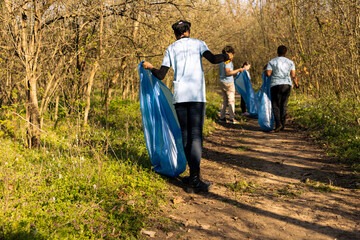 African american climate change volunteer grabbing trash in a bag, working to protect the natural...