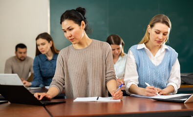 Fototapeta premium Asian and caucasian women university students sitting at table during lesson.