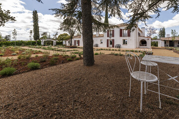 White metal table with chairs in the shade between gardens with terracotta floors and gravel in the...