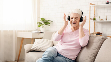 Senior woman listening to her favourite music through big headphones, enjoying rich sound, empty...