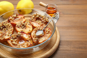 Tasty baked quinces with walnuts and honey in bowl on wooden table, closeup. Space for text