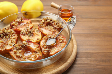 Tasty baked quinces with walnuts and honey in bowl on wooden table, closeup. Space for text