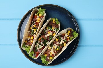 Delicious tacos with meat and vegetables on light blue table, top view