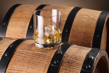 Whiskey with ice cubes in glass on wooden barrel, closeup