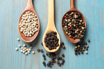 Aromatic spice. Different peppers in spoons on light blue wooden table, flat lay