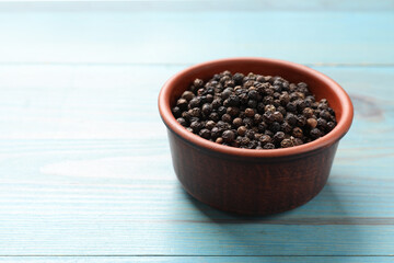 Aromatic spice. Black pepper in bowl on light blue wooden table, space for text