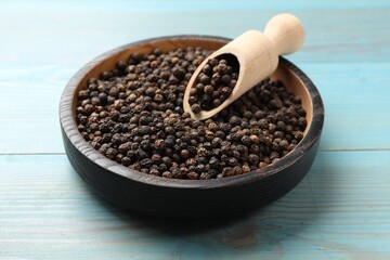 Aromatic spice. Black pepper in bowl and scoop on light blue wooden table
