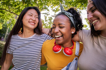 Group young multiracial female friends laughing together hugging in park on sunny day. Three...