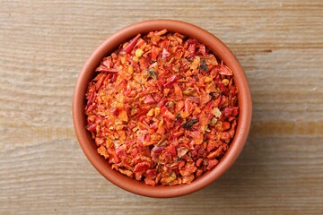 Aromatic spice. Red chili pepper flakes in bowl on wooden table, top view