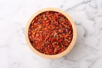 Chili pepper flakes in bowl on white marble table, top view