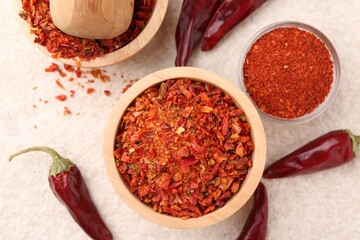 Chili pepper flakes and pods on light textured table, flat lay