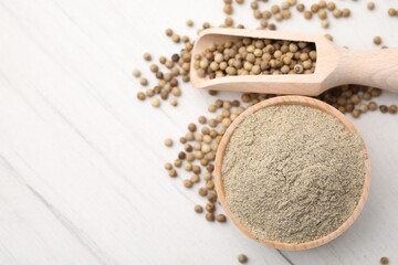 Aromatic spice. Ground pepper in bowl and scoop with peppercorns on white wooden table, flat lay. Space for text