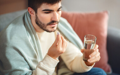 A focused young man with a short beard, wearing a casual light-colored sweater, is seated while...