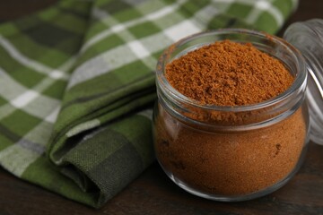 Ground red pepper in jar on wooden table, closeup