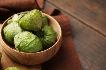 Fototapeta premium Fresh green tomatillos with husk in bowl on wooden table, closeup. Space for text