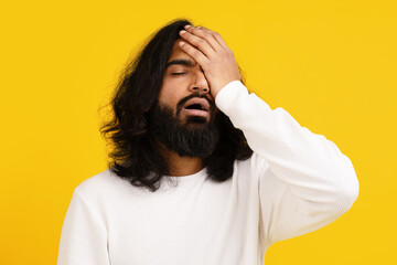 Indian young man with long dark hair and a beard appears distressed, with his eyes closed and one...