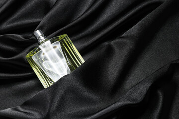 Luxury men's perfume in bottle on black satin fabric, top view. Space for text
