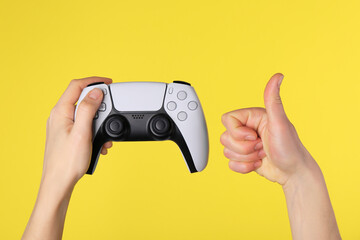 Woman with game controller showing thumbs up on yellow background, closeup