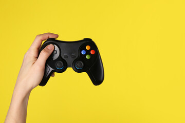 Woman using game controller on yellow background, closeup. Space for text