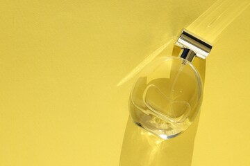 Luxury women's perfume. Sunlit glass bottle on yellow background, top view. Space for text