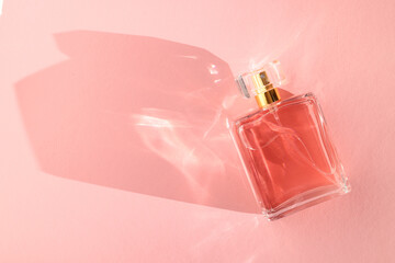 Luxury women's perfume. Sunlit glass bottle on pink background, top view. Space for text