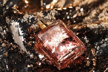 Luxury perfume in bottle on fabric with shiny sequins, closeup